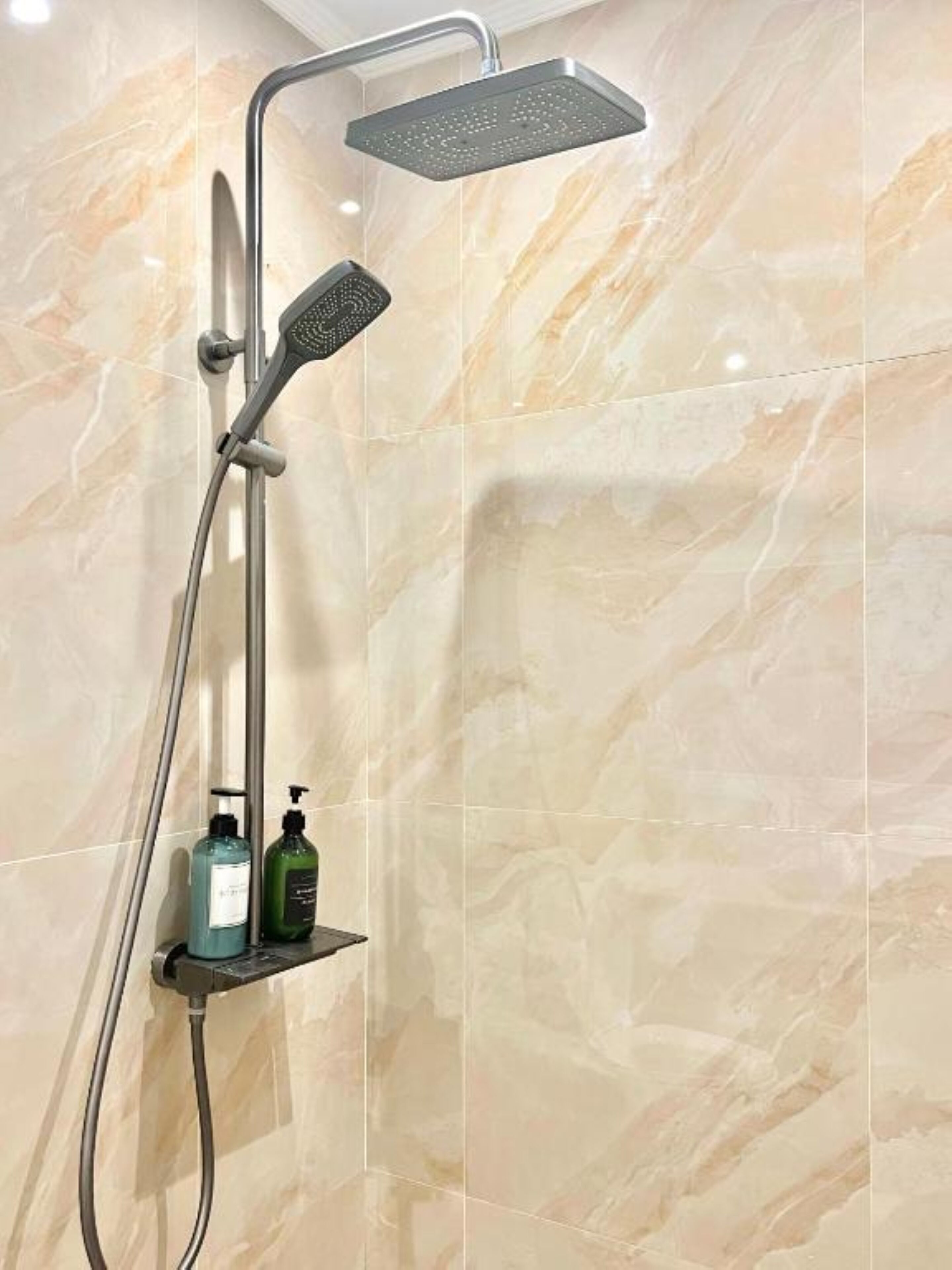 A shower with a handheld showerhead and a fixed showerhead, mounted on a wall with a marble-like tile pattern.