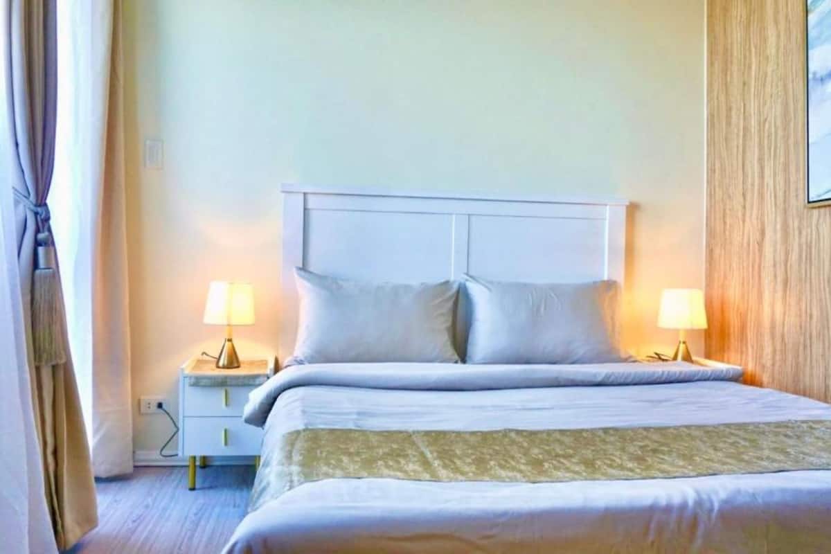 A hotel room with a bed, two bedside tables with lamps, a nightstand, and a painting on the wall.