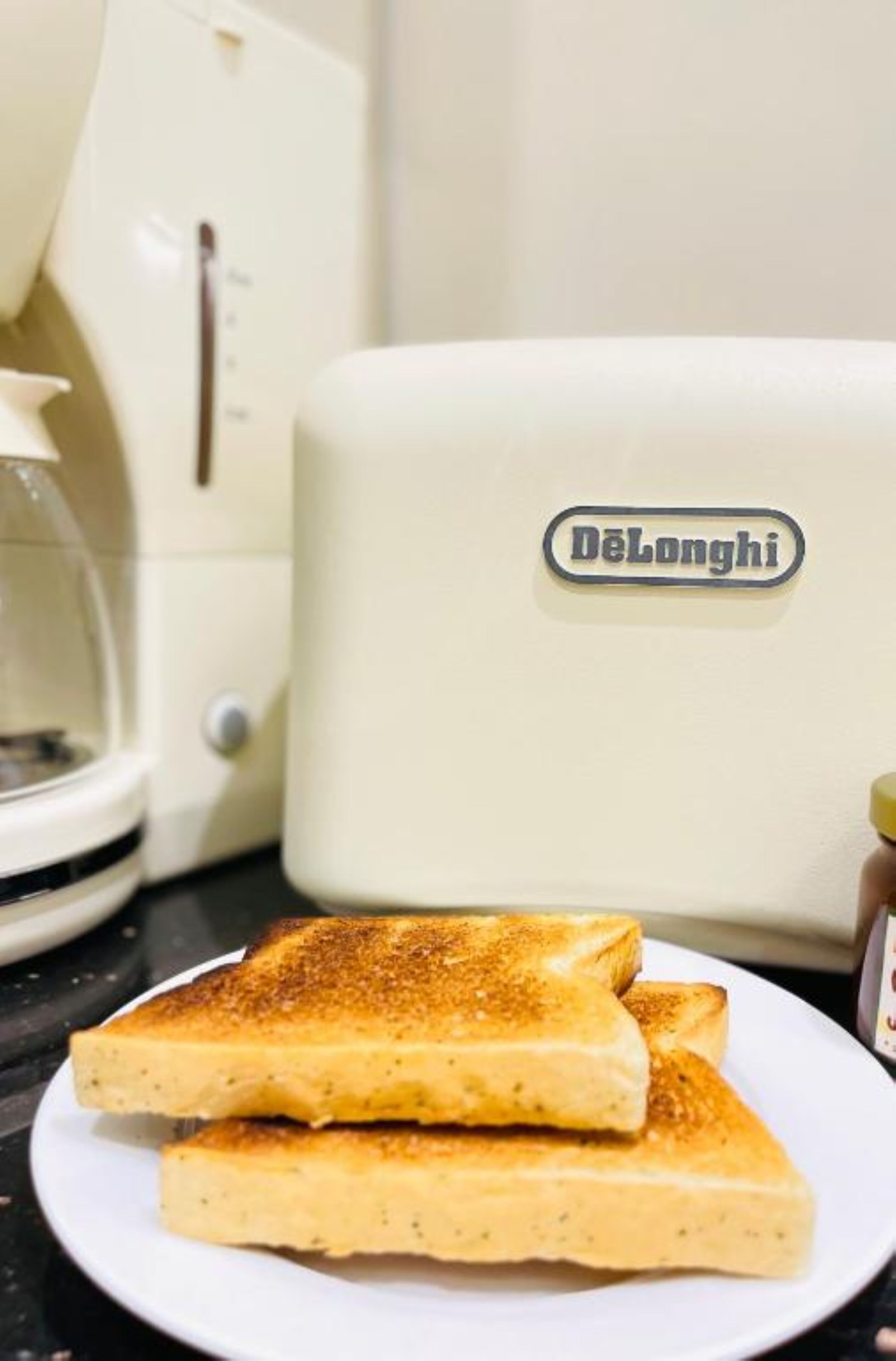 Un grille-pain DeLonghi blanc avec deux tranches de pain grillé sur une assiette.
