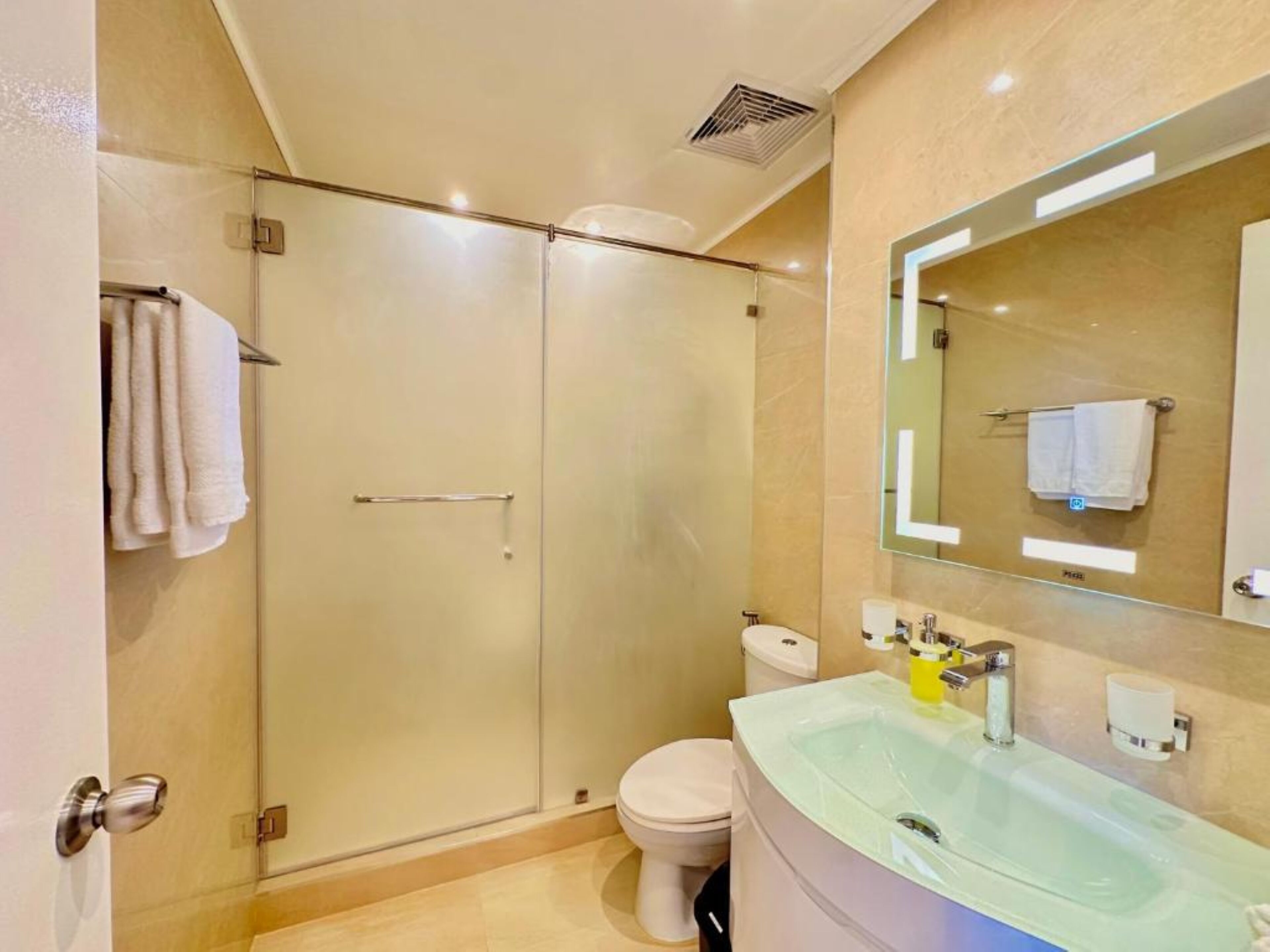 A modern bathroom with a glass-enclosed shower, a toilet, and a sink with a mirror.