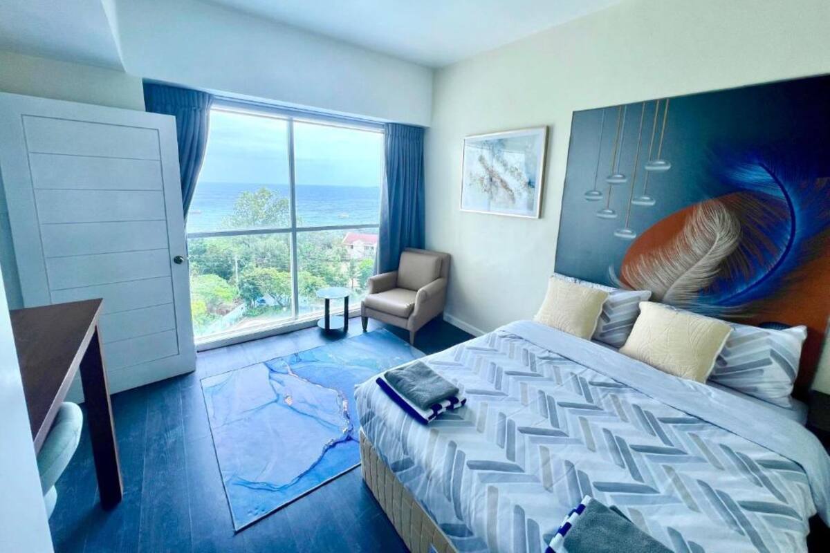 A hotel room with a large window, a bed, a chair, and a desk.
