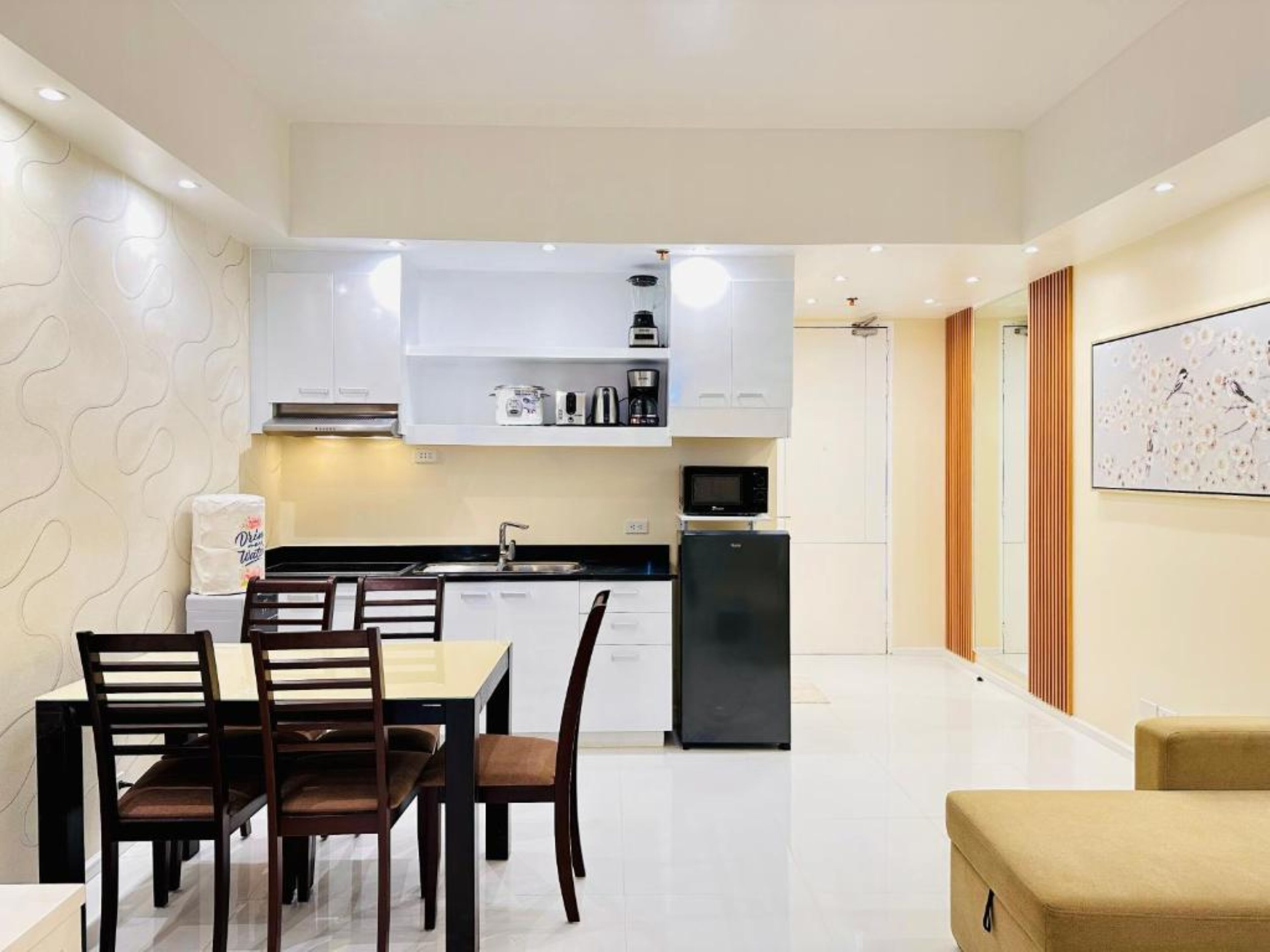 A modern kitchen with white cabinets, a black refrigerator, and a microwave. There is a dining table with chairs and a painting on the wall.