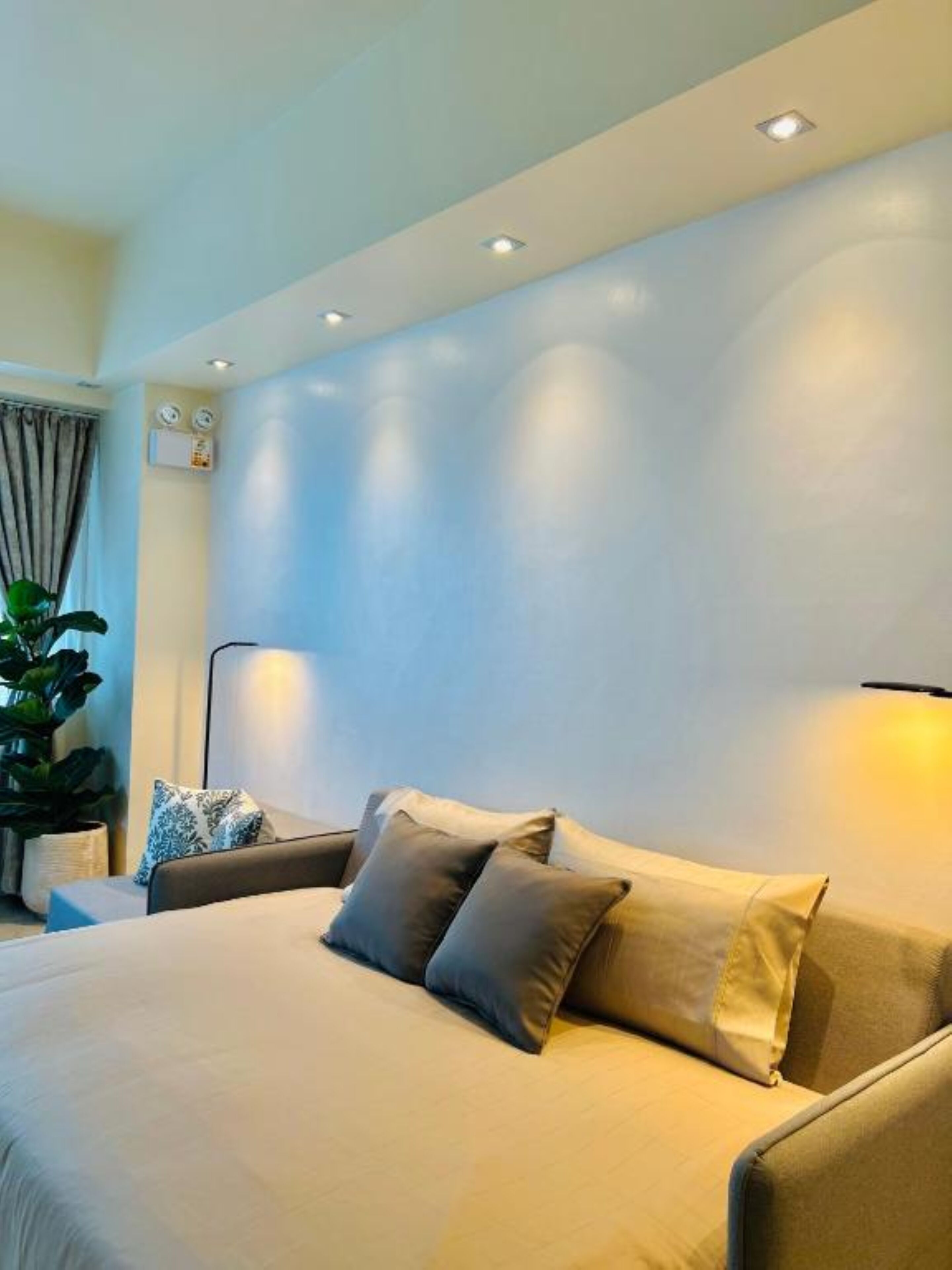 Una habitación de hotel moderna con una cama grande, una mesita de noche, una lámpara y una planta en maceta.