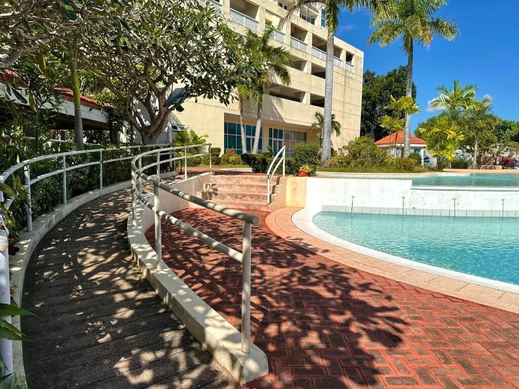 Un área de piscina con un sendero curvo, un edificio con balcones y palmeras.