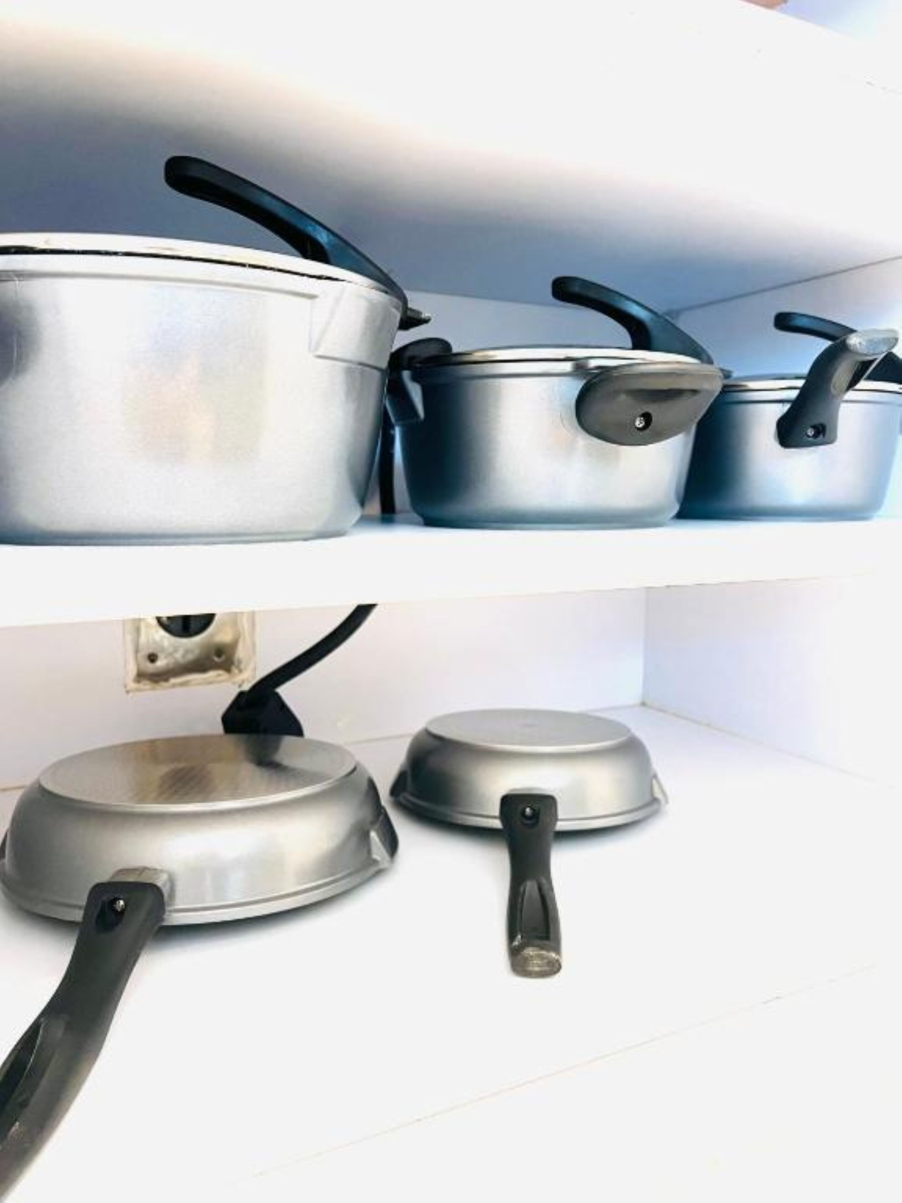 A kitchen shelf with various stainless steel pots and pans.