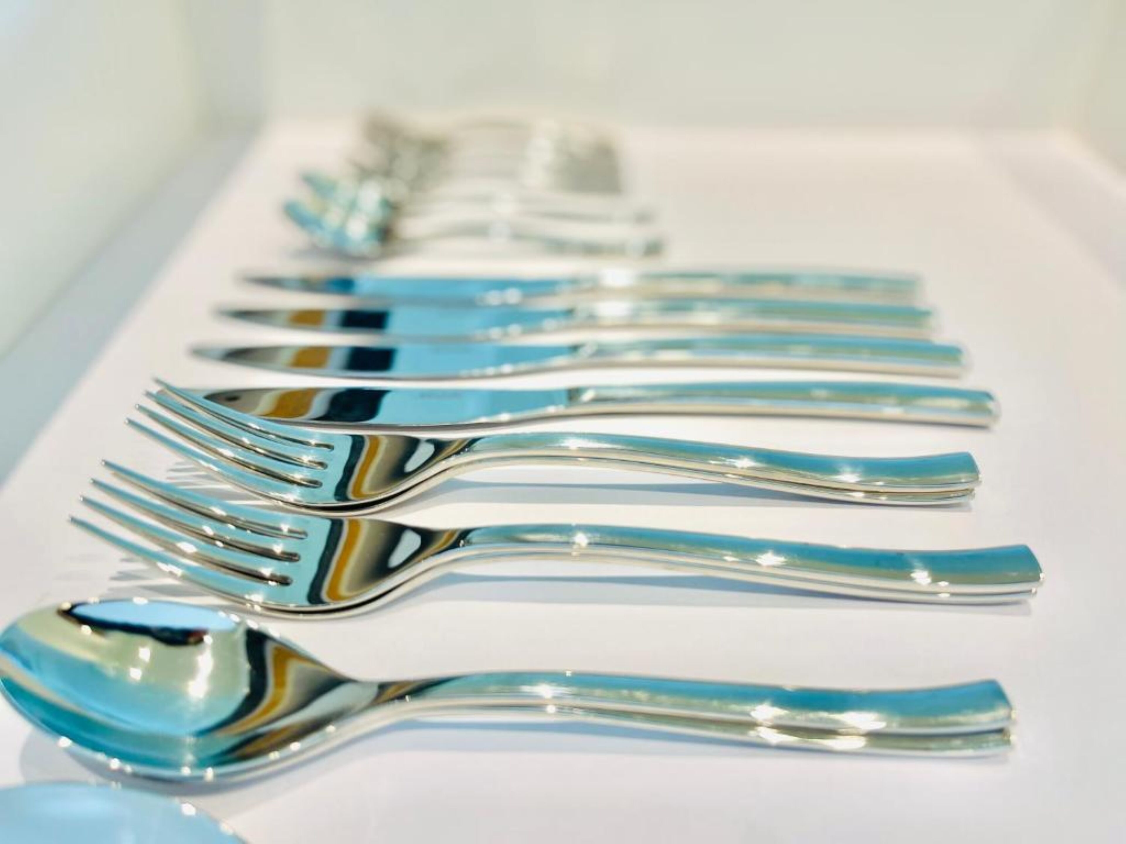 A row of silverware with blue handles on a white surface.