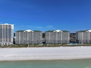 Un hotel frente a la playa con varios edificios altos, una playa arenosa y un cielo azul despejado.