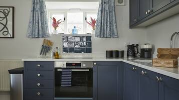 Une cuisine avec des meubles de couleur bleu foncé, un four Bosch, une fenêtre avec des rideaux et un plan de travail sur lequel sont disposés divers objets.