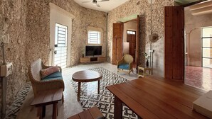 Une pièce aux murs en pierre, dotée d'un ventilateur de plafond, d'un téléviseur, de meubles en osier et d'un revêtement de sol à motifs.