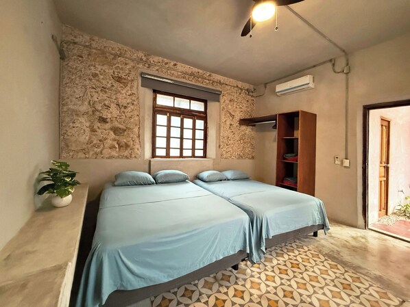 A bedroom with two beds, a stone wall, a window, and a wooden wardrobe. - Casa con Piscina Nido Rosa (Merida)