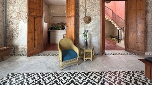 Une pièce dotée d'un sol à motifs, d'une chaise en osier, d'une petite table sur laquelle est posé un vase, et d'un escalier menant à un niveau supérieur.