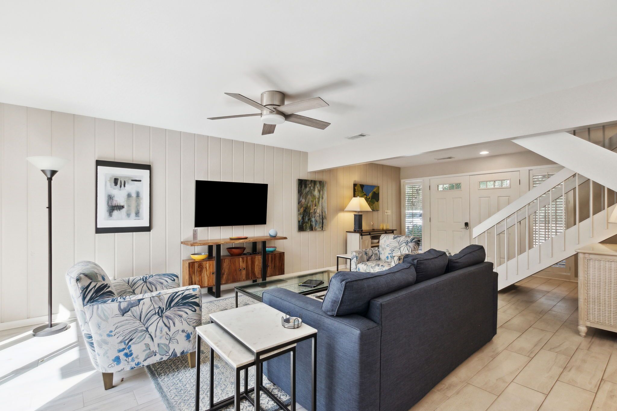 A modern living room with a sofa, coffee table, and TV. There is a staircase leading to another level.