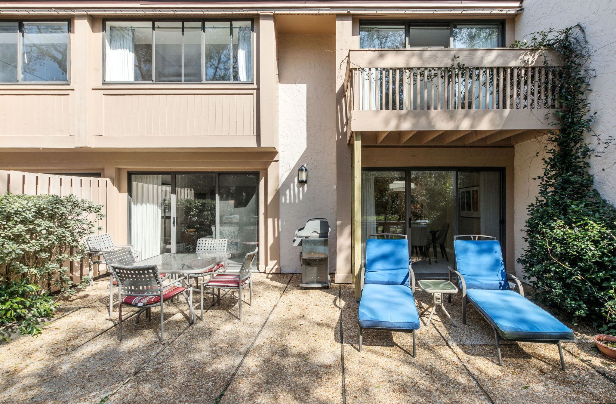 Un bâtiment à deux étages doté d’un patio aménagé avec du mobilier d’extérieur, un barbecue et un balcon orné d’une balustrade en bois.