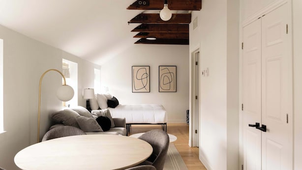 A modern living room with a round table, sofas, and a bed in the background.