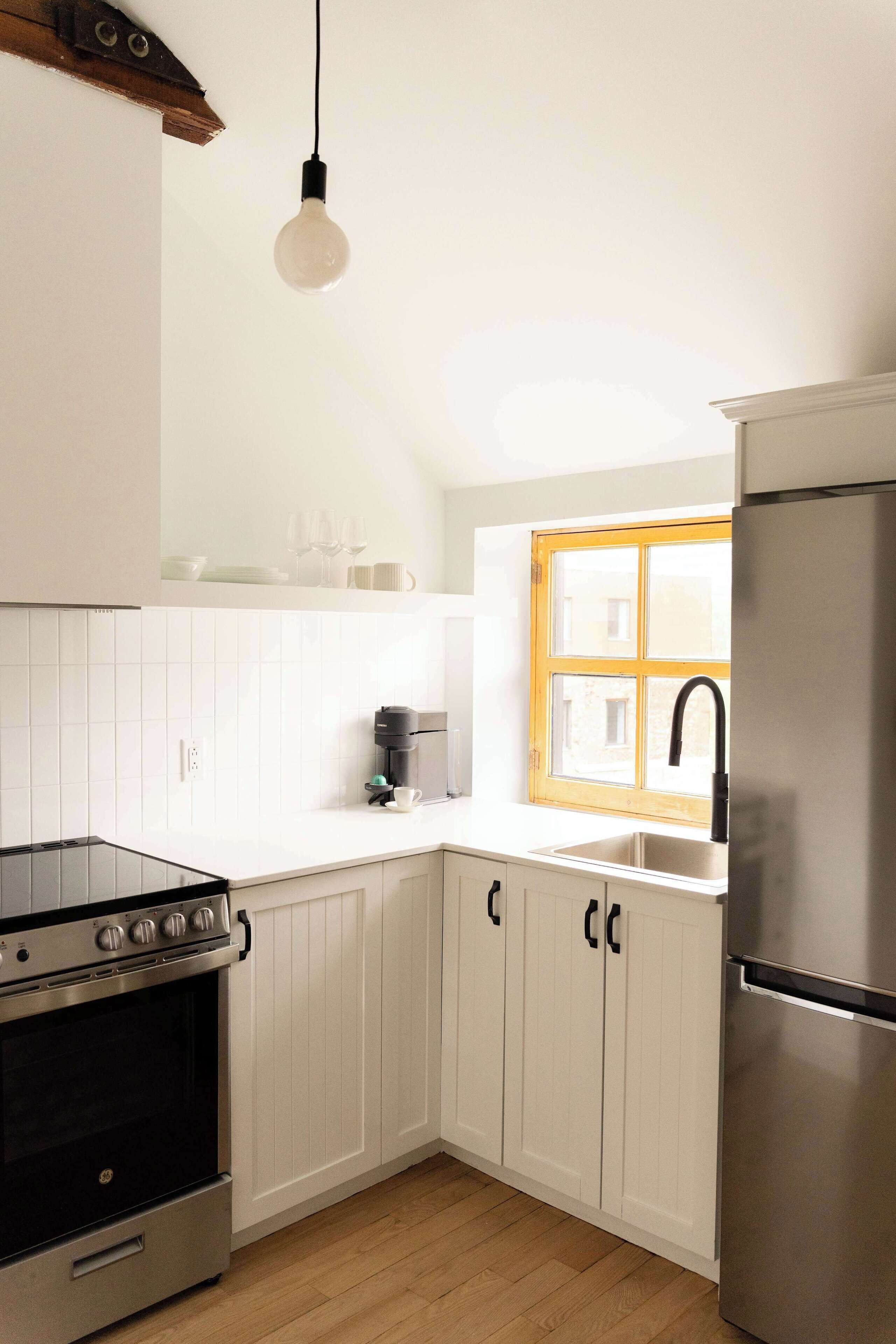 A kitchen with white cabinets, a stainless steel refrigerator, a black stove, and a window with a yellow frame.