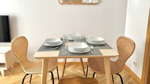 A dining area with a table set for four, surrounded by wicker chairs, a mirror on the wall, and a television in the background. - Vivodomo | Free parking, top location, modern (Madrid)