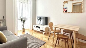 A modern living room with a sofa, a TV, a dining table with chairs, a mirror, and a potted plant. - Vivodomo | Free parking, top location, modern (Madrid)