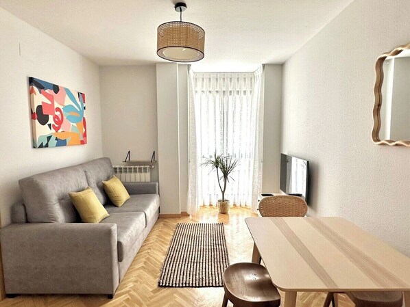 A modern living room with a sofa, a dining table, a TV, and a large window with curtains. - Vivodomo | Free parking, top location, modern (Madrid)
