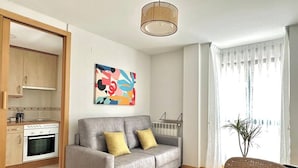A modern living room with a grey sofa, a dining table, and a kitchen area with a stove and oven. - Vivodomo | Free parking, top location, modern (Madrid)