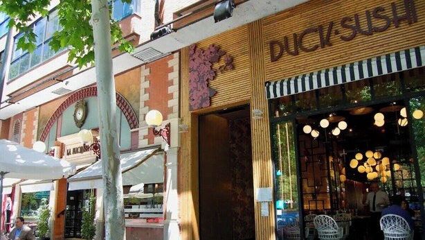 A restaurant named Duck Sushi with a wooden facade and large windows displaying hanging lights. - Vivodomo | Free parking, top location, modern (Madrid)