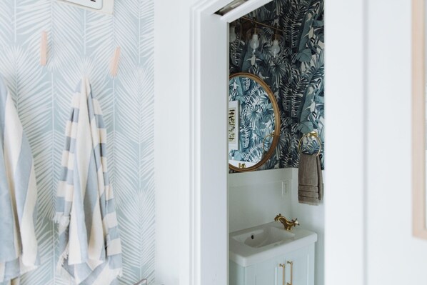 A bathroom with a white sink, gold faucet, and a mirror with a blue and white leaf pattern.