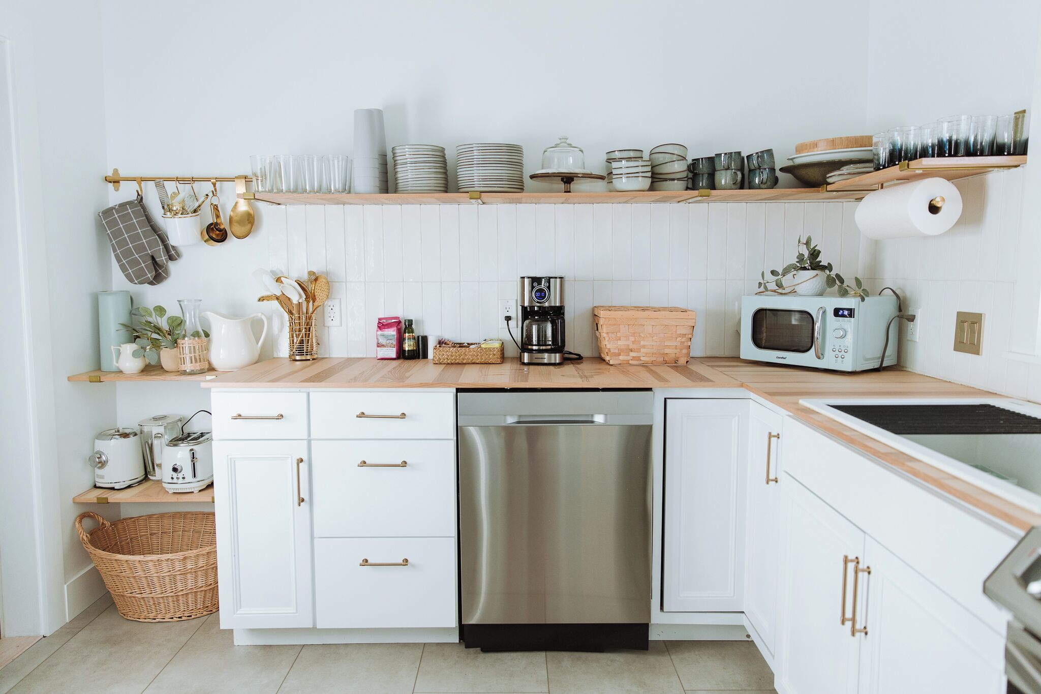 Una cocina moderna con armarios blancos, un lavavajillas de acero inoxidable, un microondas y una cafetera.