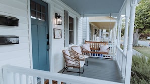 A porch with wicker chairs and a wooden bench, a blue door, and a white railing. - Walk to Dining, Beach & Park~Family Friendly Home! (Cape Charles)