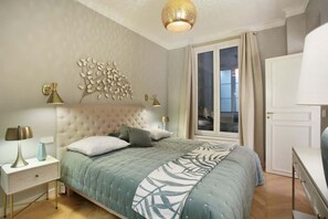 A bedroom with a tufted headboard, a large bed with a leaf-patterned bedspread, bedside lamps, and a window with curtains. - Sublime apartment Center of Paris Opera Madeleine (Paris)