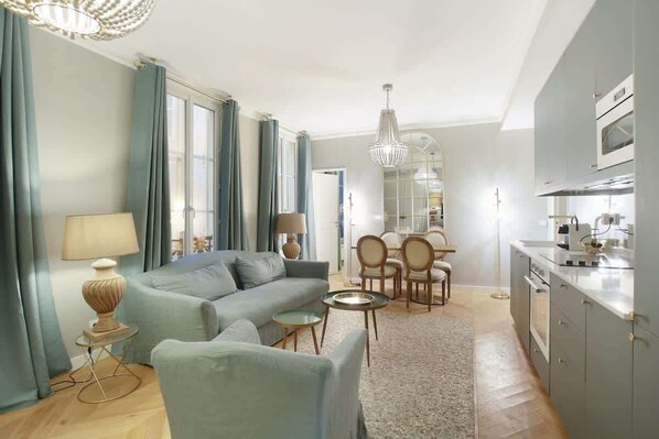 A modern living room with a sofa, chairs, a dining table, and a kitchen area with cabinets and appliances. - Sublime apartment Center of Paris Opera Madeleine (Paris)