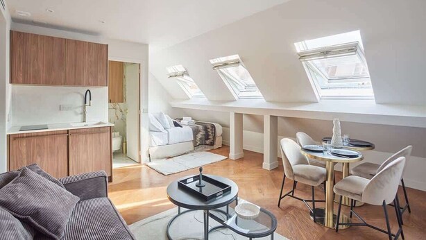 Un appartement moderne comprenant une cuisine, un coin repas et un salon avec un canapé et une table basse. Des puits de lumière permettent de bénéficier d’un éclairage naturel.