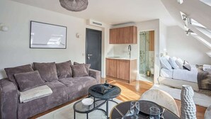 Un salon moderne avec un canapé gris, une table basse et un coin repas comprenant une petite table et des chaises. On y trouve également une cuisine avec des meubles en bois et un évier.