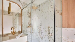 Une salle de bain moderne avec un mur de douche en marbre, un robinet doré et une douche à parois de verre.
