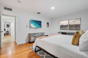 A bedroom with a large bed, a TV, a dresser, and a window with blinds.
