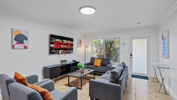 Een moderne woonkamer met grijze banken, een salontafel en een flatscreen televisie aan de muur.