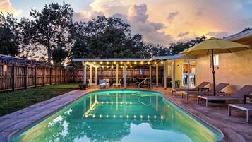 Un jardin avec une piscine, un patio couvert agrémenté d’étagères et un jardin clos.