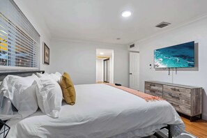 A bedroom with a large bed, a TV mounted on the wall, and a wooden dresser.