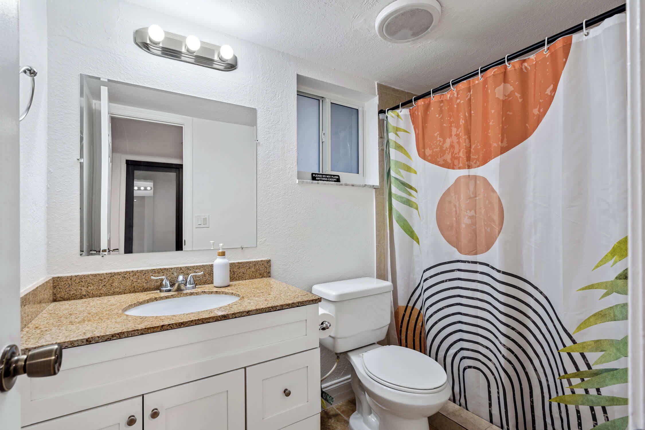 A bathroom with a white sink, a mirror, a toilet, and a shower curtain with a leaf pattern.