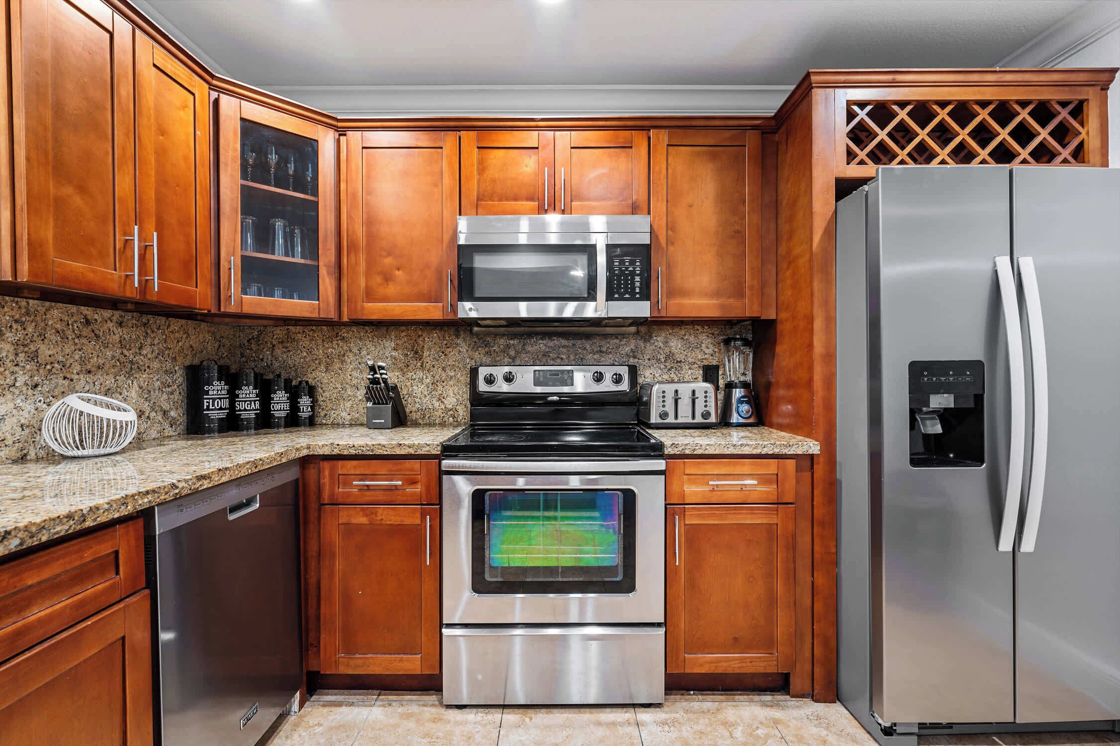 Una cocina con gabinetes de madera, electrodomésticos de acero inoxidable, incluyendo un microondas, horno y refrigerador, y encimeras de granito.