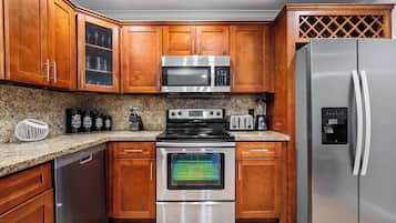 Una cocina con gabinetes de madera, electrodomésticos de acero inoxidable, incluyendo un microondas, horno y refrigerador, y encimeras de granito.