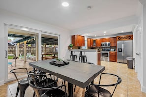 A modern kitchen with wooden cabinets, a stainless steel refrigerator, and a dining area with a table and chairs.