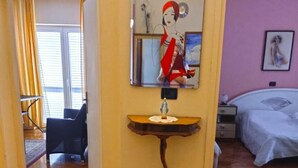 A hotel room with a wooden floor, a bed with a white cover, a bedside table with a lamp, a wall-mounted mirror, and a framed picture. - Charming Apartment in Umag With Balcony (Umag)