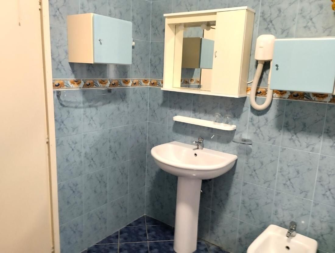 A bathroom with a pedestal sink, a mirror, a small cabinet, and a bidet.