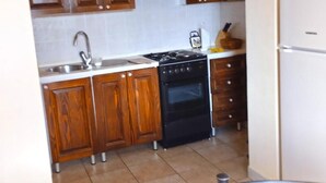 A kitchen with wooden cabinets, a stainless steel sink, a black stove, and a white refrigerator. - Charming Apartment in Umag With Balcony (Umag)