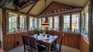 Un comedor con paredes de madera, ventanas grandes con vidrio decorativo y una araña.