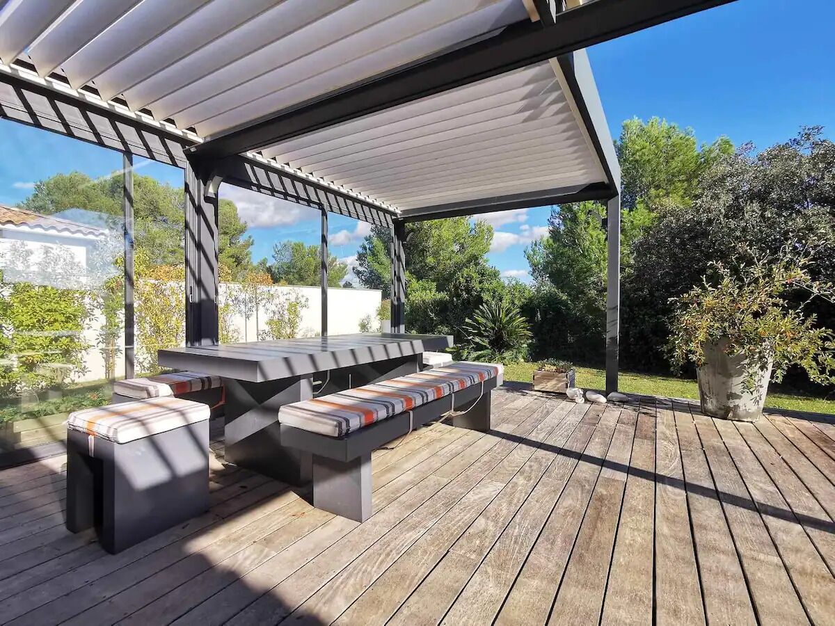 Una veranda esterna con zona salotto coperta, barbecue e una pianta in vaso.