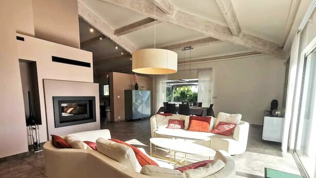 Een moderne woonkamer met een open haard, witte banken en een eethoek op de achtergrond.