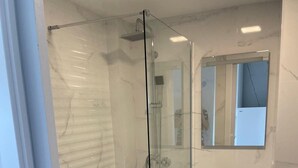 Un baño moderno con ducha de vidrio, lavamanos blanco y espejo sobre el mueble.