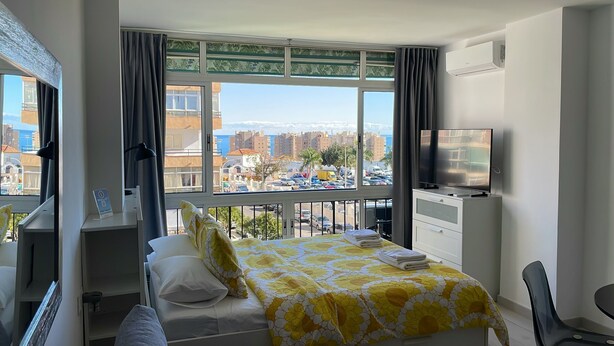 A hotel room with a bed, a TV, a desk, and a window with a city view.