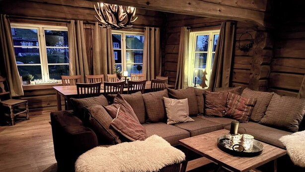 Un acogedor interior de cabaña de madera con un amplio sofá de madera, un otomano mullido y una mesa de centro de madera.