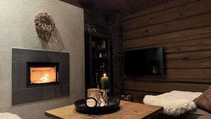 Interior acogedor de una cabaña de troncos con chimenea, un televisor de pantalla plana y una mesa de madera con una vela y elementos decorativos.